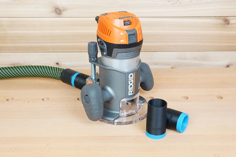 May include: A gray and orange RIDGID router with a clear base, a green and black hose, and two black and blue accessories. The router is on a light wood surface.