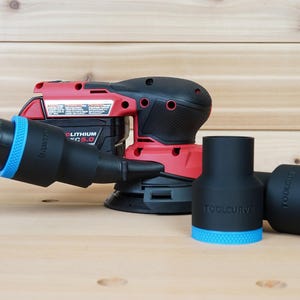 Puede incluir: Una lijadora inalámbrica roja y negra con una manguera negra y adaptadores negros con detalles azules. Los adaptadores tienen el texto "TOOLCURVE" impreso. La lijadora está sobre una superficie de madera marrón claro.
