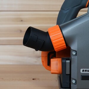 May include: Close-up of a gray and orange power tool with a black dust port. The tool has a label that says "BRUSHLESS".