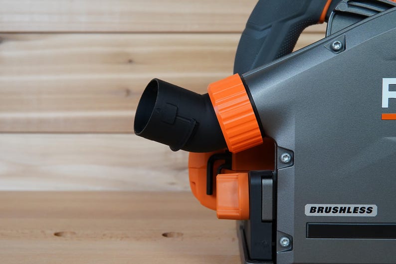 May include: Close-up of a gray and orange power tool with a black dust port. The tool has a label that says "BRUSHLESS".