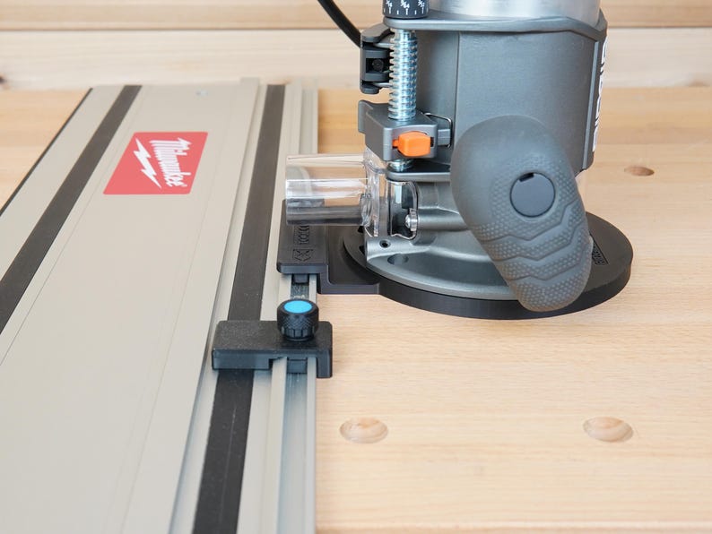 May include: A gray and black power router with a black handle and a silver guide rail. The guide rail has a red and white Milwaukee logo. The router is on a light wood surface.