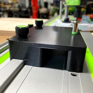 以下が含まれることがあります： 緑色のノブと銀色のピンが付いた黒いプラスチック製のジグ。ジグは緑色のラインが付いた銀色のトラックに取り付けられています。