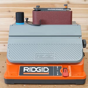 May include: A gray and orange belt sander with a dust collection port and a red on/off switch. The sander is labeled "RIDGID".