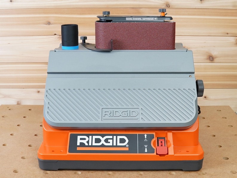 May include: A gray and orange belt sander with a dust collection port and a red on/off switch. The sander is labeled "RIDGID".