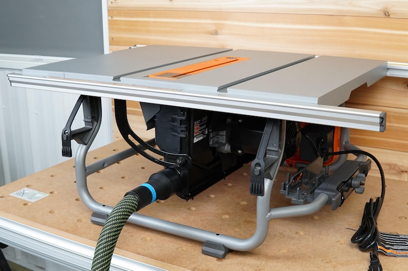 May include: A grey table saw with a black motor and a grey metal stand. The saw has a black and orange power cord and a black and blue dust collection hose.