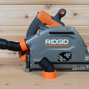 May include: A gray and orange Ridgid circular saw with a dust collection port and a black hose attached. The saw has a clear plastic window to view the blade and a black and orange dust collection adapter.