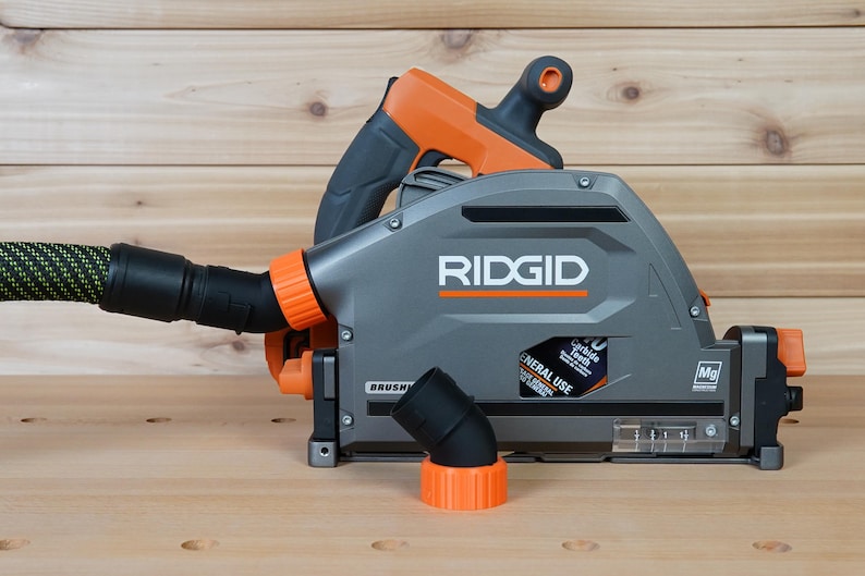 May include: A gray and orange Ridgid circular saw with a dust collection port and a black hose attached. The saw has a clear plastic window to view the blade and a black and orange dust collection adapter.