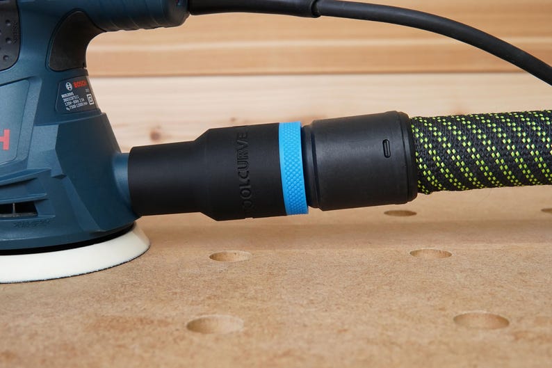 Peut inclure: Une ponceuse &eacute;lectrique bleue et noire avec un tuyau d'aspiration des poussi&egrave;res. Le tuyau est noir avec un rev&ecirc;tement en tissu &agrave; motifs vert et jaune. La ponceuse a un port d'aspiration des poussi&egrave;res bleu et noir avec le mot "ROL-CURVE" imprim&eacute; dessus.
