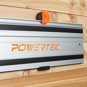 Puede incluir: Un sistema de rieles de pared de metal plateado y negro con la palabra "POWERTEC" impresa en naranja. El riel tiene dos clips de plástico negro a los lados.