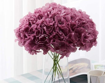 May include: A bouquet of artificial purple hydrangeas in a clear glass vase. The vase is sitting on a light blue and white checked tablecloth.