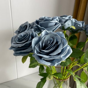 May include: A bouquet of dusty blue silk roses with green leaves in a clear glass vase.