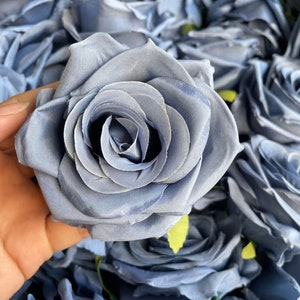 Può includere: Un mazzo di rose artificiali di seta di colore azzurro chiaro. Le rose sono disposte in primo piano, mostrando i dettagli delicati dei petali di tessuto.