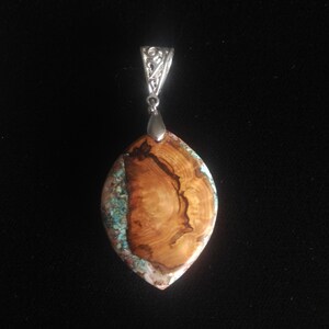 May include: A pendant with a silver bail and a large, oval-shaped stone. The stone features a striking combination of wood grain and turquoise, with a polished finish. The pendant is a unique piece of jewelry.