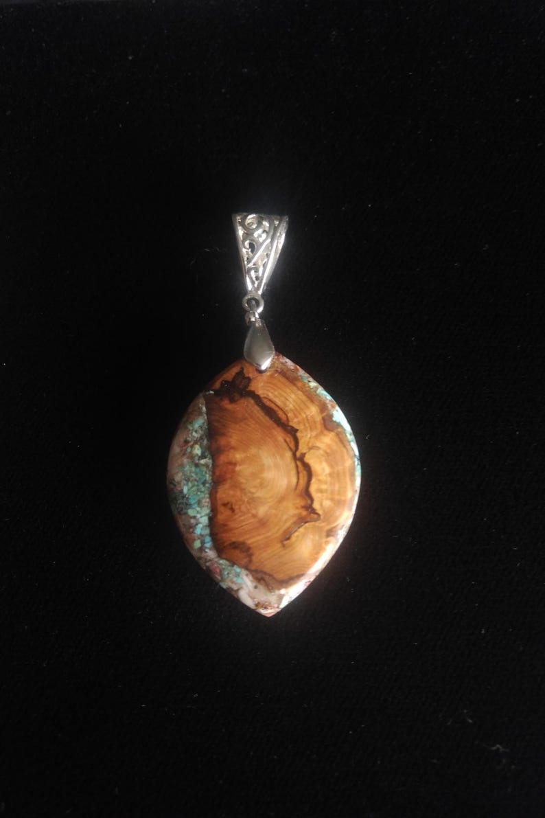 May include: A pendant with a silver bail and a large, oval-shaped stone. The stone features a striking combination of wood grain and turquoise, with a polished finish. The pendant is a unique piece of jewelry.