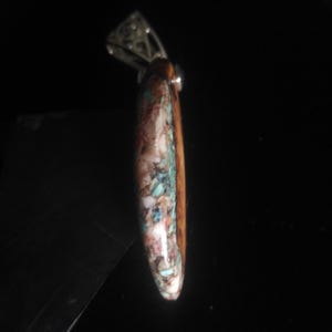 May include: A pendant with a silver bail and a teardrop-shaped stone. The stone features a mosaic of colors, including brown, white, turquoise, and pink. The pendant is likely for a necklace.