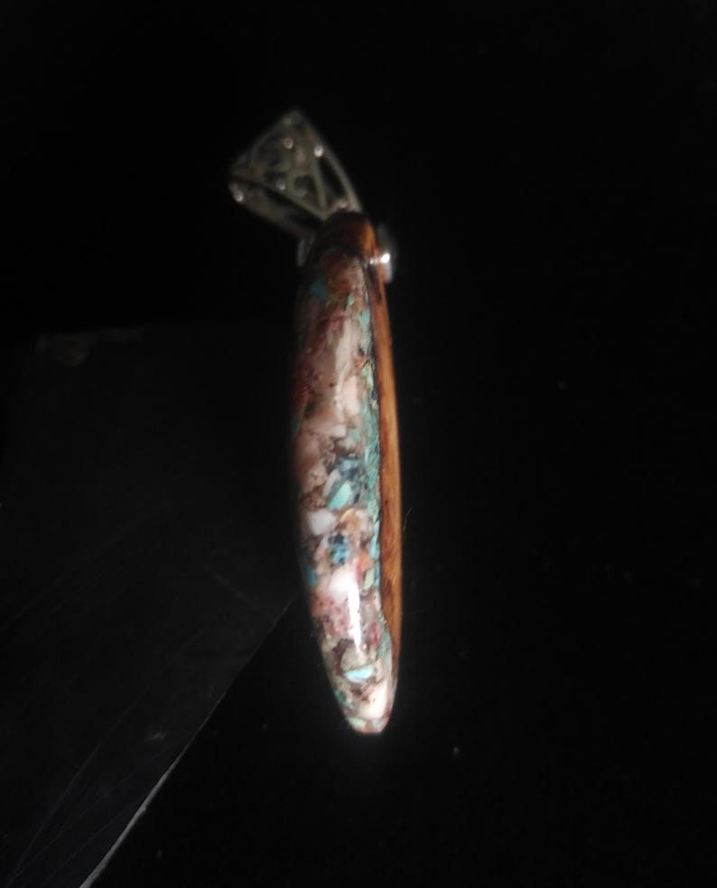 May include: A pendant with a silver bail and a teardrop-shaped stone. The stone features a mosaic of colors, including brown, white, turquoise, and pink. The pendant is likely for a necklace.