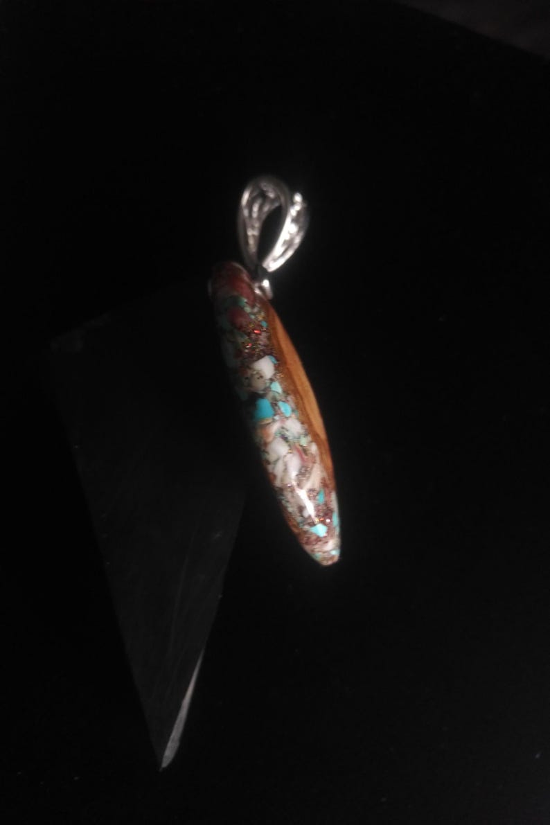 May include: A pendant with a silver bail and a teardrop-shaped stone. The stone features a mosaic pattern of brown, white, turquoise, and red-orange colors. The pendant is likely a piece of jewelry.