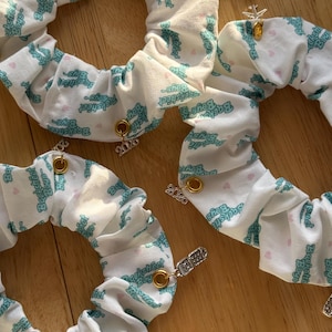 May include: White scrunchies with a teal "Backstreet Boys" logo print and small heart accents. Each scrunchie has a gold-colored grommet and a charm, some with the year "2020".