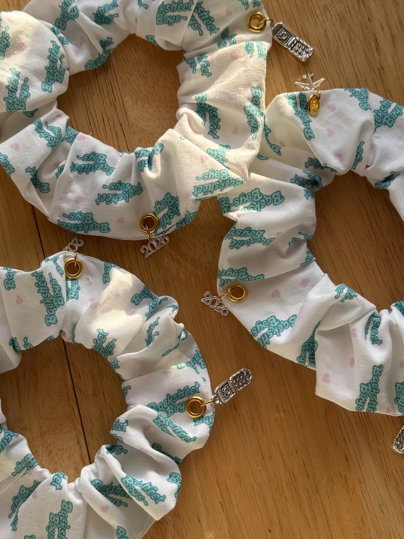 May include: White scrunchies with a teal "Backstreet Boys" logo print and small heart accents. Each scrunchie has a gold-colored grommet and a charm, some with the year "2020".