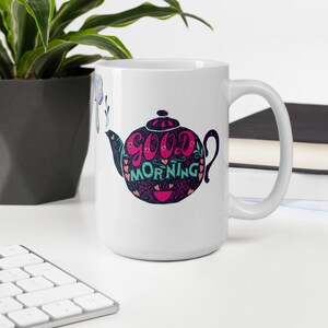 May include: White ceramic coffee mug featuring a black and white illustration of a teapot with the words "good morning" in pink and teal lettering.