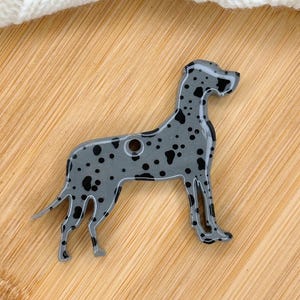 May include: A gray and black Great Dane dog shaped charm with black spots. The charm is made of resin and has a hole for hanging.