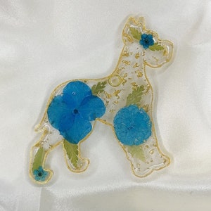 May include: A clear resin dog charm with gold glitter and pressed blue flowers. The dog is a Great Dane breed.