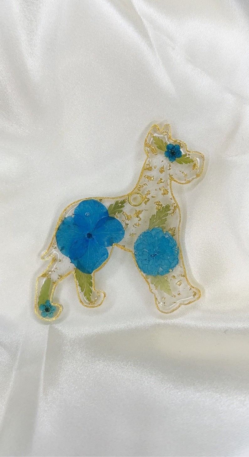 May include: A clear resin dog charm with gold glitter and pressed blue flowers. The dog is a Great Dane breed.