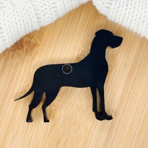 May include: Black silhouette of a Great Dane dog, cut from wood, with a hole for hanging. The silhouette is on a light brown wooden surface.