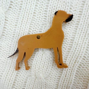 May include: A brown wooden cutout of a dog, possibly a Great Dane, with black markings on its head. The cutout is on a white knitted surface.