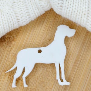 May include: White wooden cutout of a Great Dane dog. The cutout is standing on a light brown wooden surface.