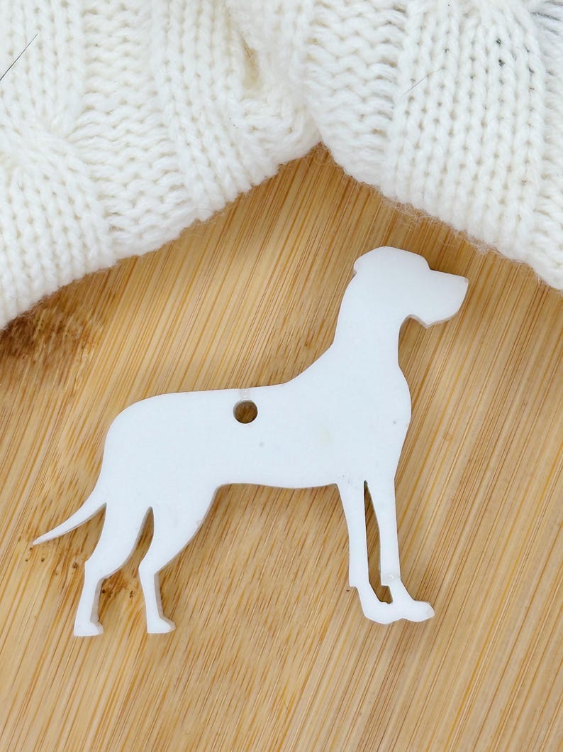 May include: White wooden cutout of a Great Dane dog. The cutout is standing on a light brown wooden surface.