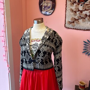 May include: A mannequin displays a black and white patterned jacket over a white t-shirt with the word "EVER" and a red skirt. The jacket has a geometric design. The skirt is a solid red with a checkered trim.