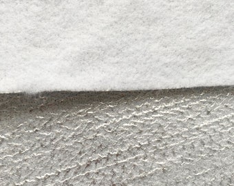 May include: Close-up of a white, fluffy fabric layered over a textured, gray surface. The top layer is a soft, cloud-like material, while the bottom has a rough, uneven appearance. The contrast highlights the different textures.