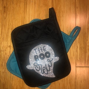 Puede incluir: Manopla de horno negra con diseño acolchado y un fantasma de purpurina plateada con el texto "The Boo Crew".