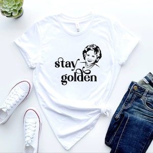 May include: White t-shirt with a black graphic of a woman with curly hair and the text "stay golden".