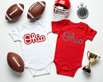 May include: Two white and red baby onesies with the word "Ohio" in red and gray lettering. The onesies are surrounded by footballs, a football helmet, and a stopwatch.