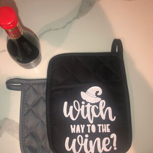 May include: A black and gray oven mitt with the text "witch way to the wine?" in white. A witch's hat graphic is above the text.