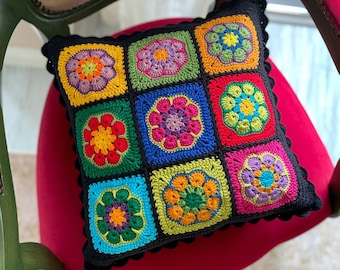 Könnte beinhalten: Ein farbenfrohes gehäkeltes Kissen mit schwarzem Rand und floralem Muster. Das Kissen besteht aus Quadraten mit verschiedenen farbigen Blumen in jedem Quadrat.