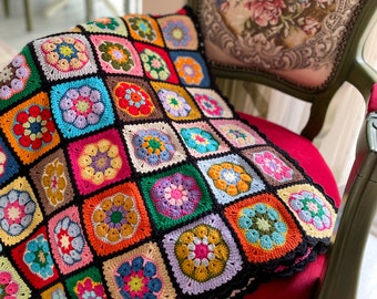 May include: A colorful crocheted blanket with a black background and a floral pattern. The blanket is made of squares with different colored flowers in the center. The blanket is draped over a chair.