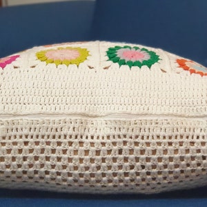K&ouml;nnte beinhalten: Ein wei&szlig;es H&auml;kelkissen mit Rei&szlig;verschluss und bunten Blumendesigns.