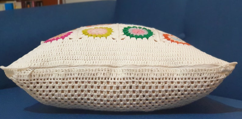 K&ouml;nnte beinhalten: Ein wei&szlig;es H&auml;kelkissen mit Rei&szlig;verschluss und bunten Blumendesigns.