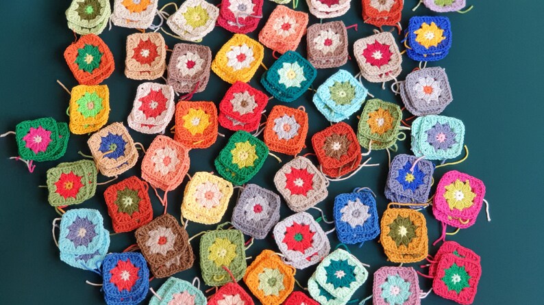 May include: A collection of colorful crocheted squares with various floral patterns. The squares are arranged in a semi-circle on a green background.