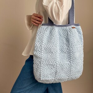 Puede incluir: Un bolso tote de crochet azul claro con una correa azul oscuro. El bolso est&aacute; hecho con un patr&oacute;n de puntadas texturizadas.