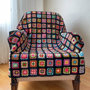 Puede incluir: Una manta de crochet negra con cuadrados de granny coloridos, drapeada sobre un sillón beige con patas de madera.