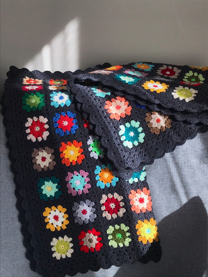 May include: A colorful granny square crochet blanket with a dark gray background. The blanket is made up of many different colored squares, including red, orange, yellow, green, blue, and purple.