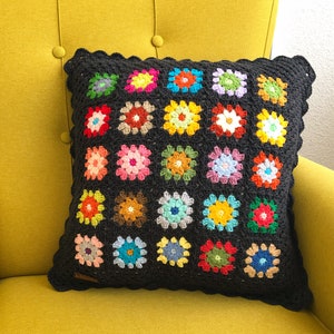 May include: A black crochet pillow with a scalloped edge and a colorful floral pattern. The pillow is made of multiple squares with different colored flowers in each square.