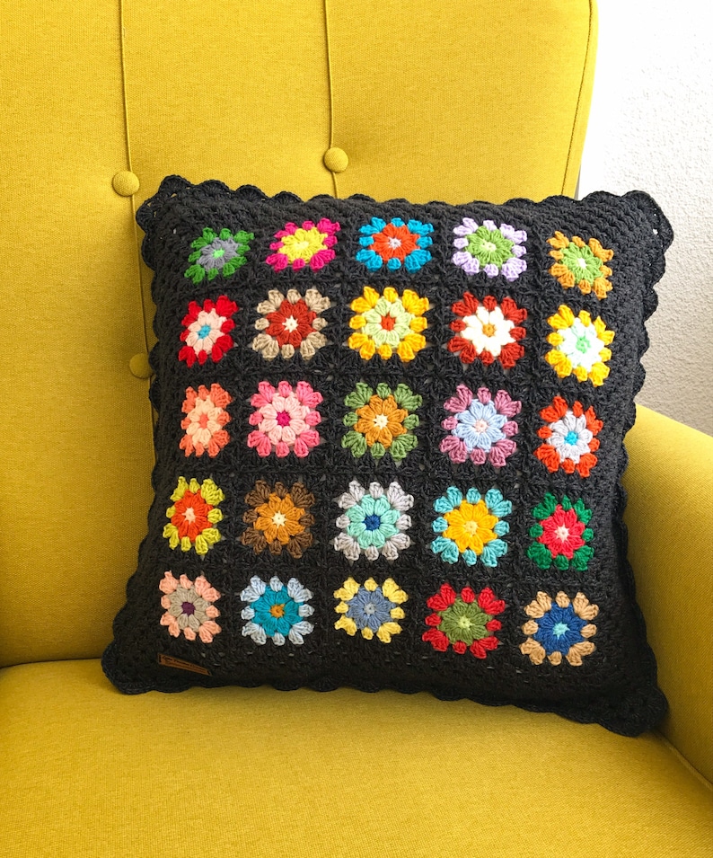 May include: A black crochet pillow with a scalloped edge and a colorful floral pattern. The pillow is made of multiple squares with different colored flowers in each square.