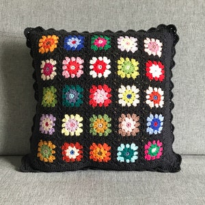 May include: A black crocheted pillow with a square pattern of colorful flowers. The pillow has a scalloped edge.