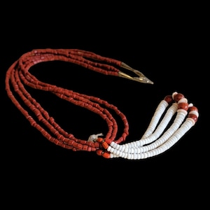 May include: A multi-strand necklace featuring red and white beads. The necklace has four strands of red beads and four strands of white beads with red accents. The necklace has a gold-colored clasp and is set against a black background.
