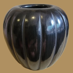 May include: A glossy black ceramic vase with a rounded, ribbed body. The vase has a wide opening and a smooth, reflective surface. The dark color and unique shape give it a modern, artistic feel. This decorative piece is suitable for home decor.